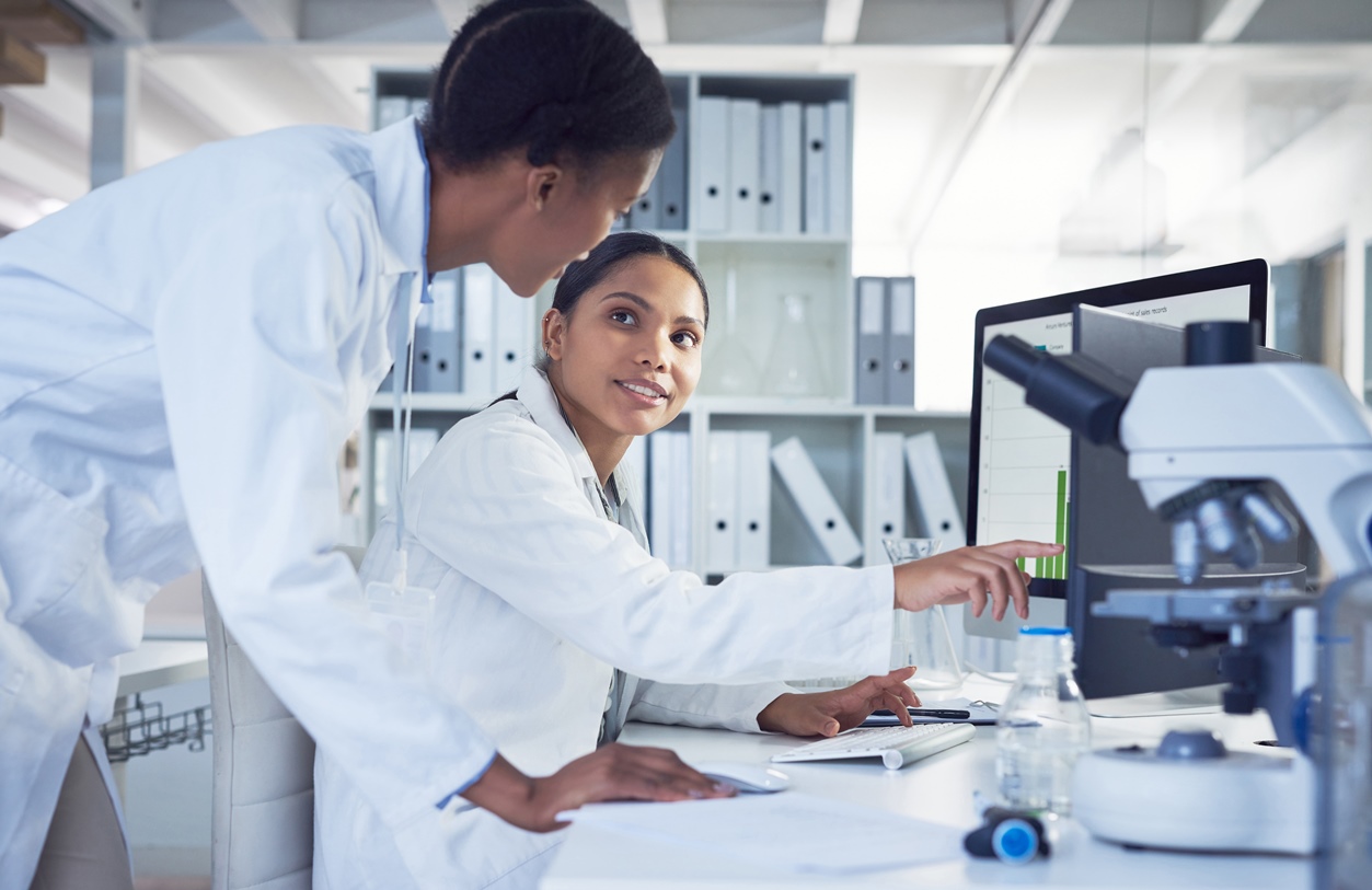 Two scientists working together to use a lab informatics platform on a computer in a lab